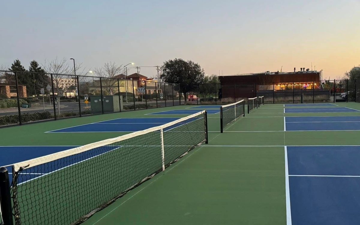 Dedicated pickleball courts at the South Napa Century Center at dusk, nets up and the lit centre beyond the fence