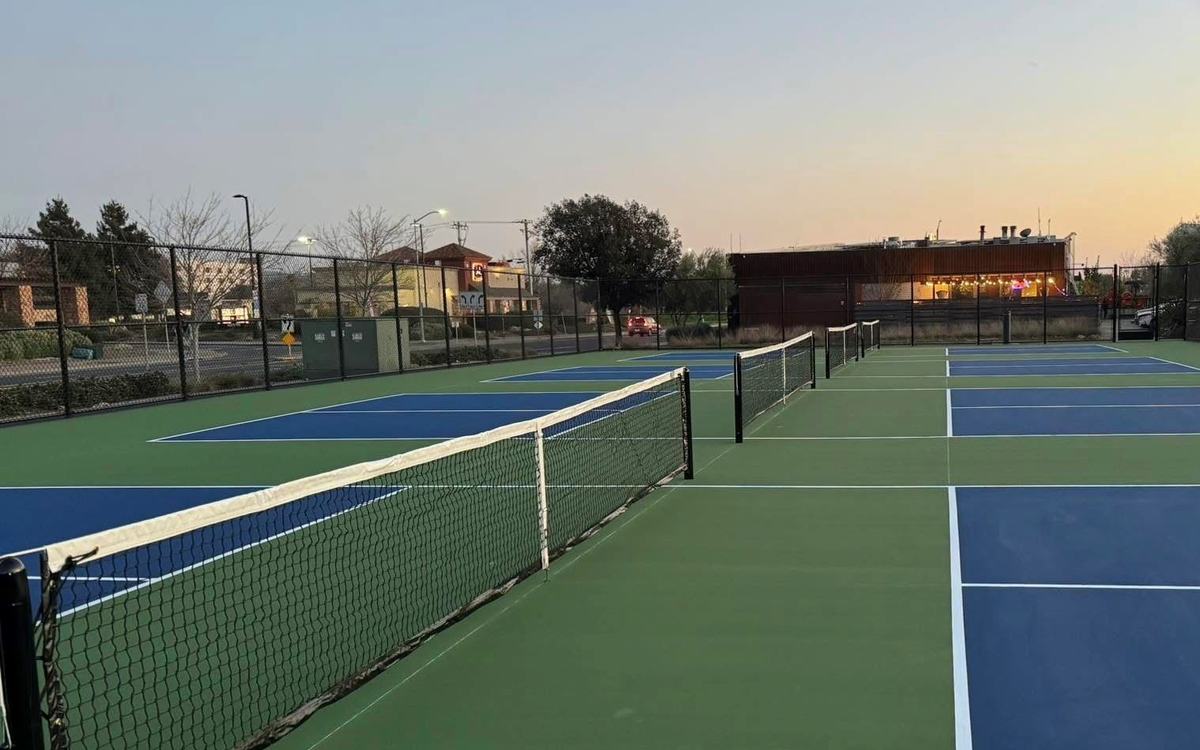 Dedicated pickleball courts at the South Napa Century Center at dusk, nets up and the lit center beyond the fence