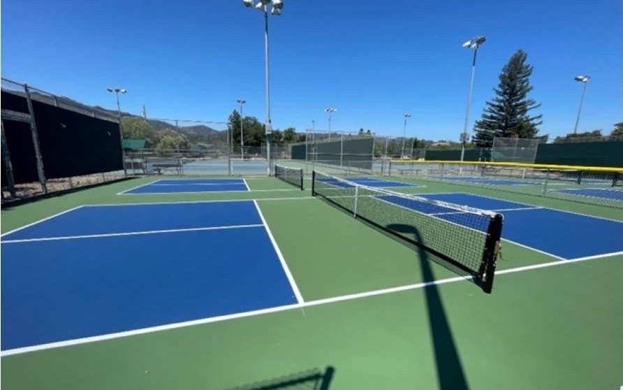 The dedicated pickleball courts at Crane Park, St. Helena, with floodlights, green windscreens and hills behind
