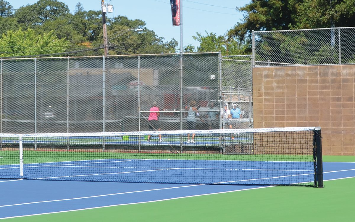 Resurfaced blue and green hard courts at Howarth Memorial Park, Santa Rosa, with a net in the foreground and players courtside behind the fence