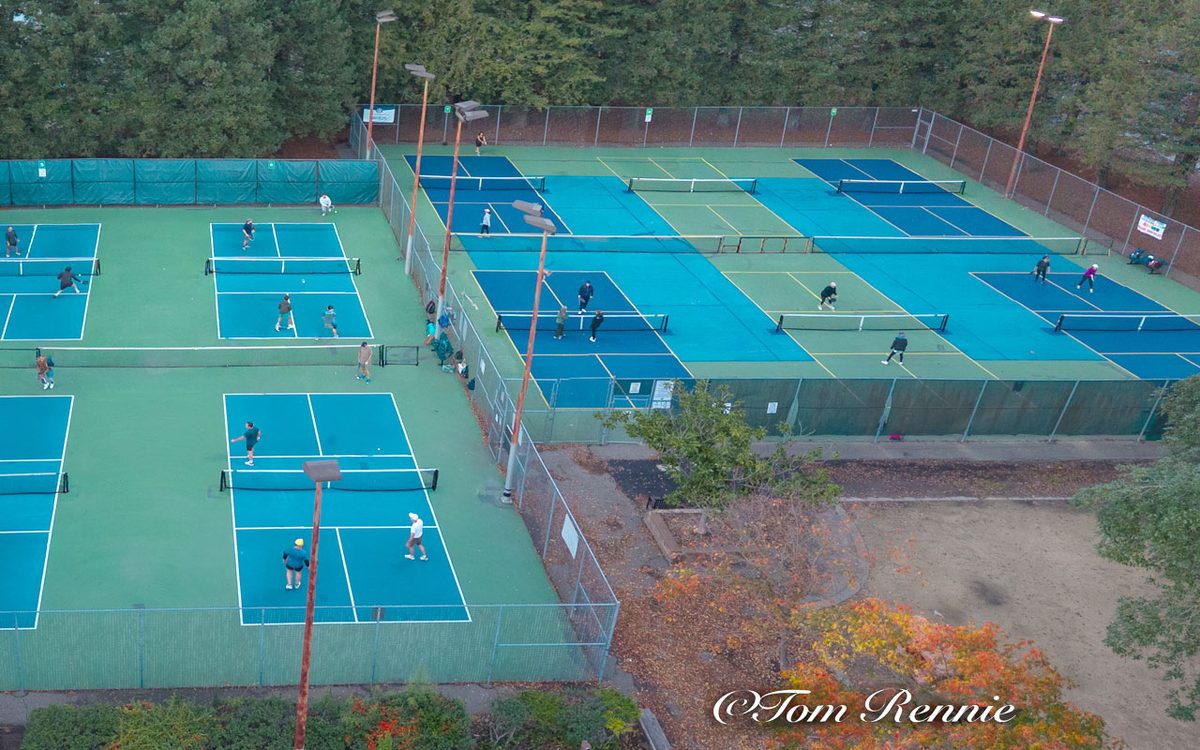 Aerial view of the twelve outdoor pickleball courts at Sunrise Park, Rohnert Park, busy with doubles games under floodlights at dusk